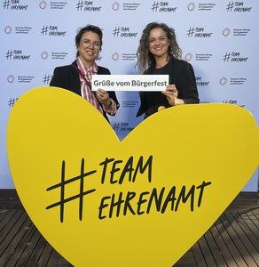 zwei Frauen hinter gelben Herz mit Aufschrift Team Ehrenamt